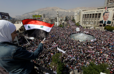 Seorang pendukung Bashar Assad mengibarkan bendera negara ke arah ribuan pendukung pemerintah lainnya di kota Damaskus, Maret 2011.